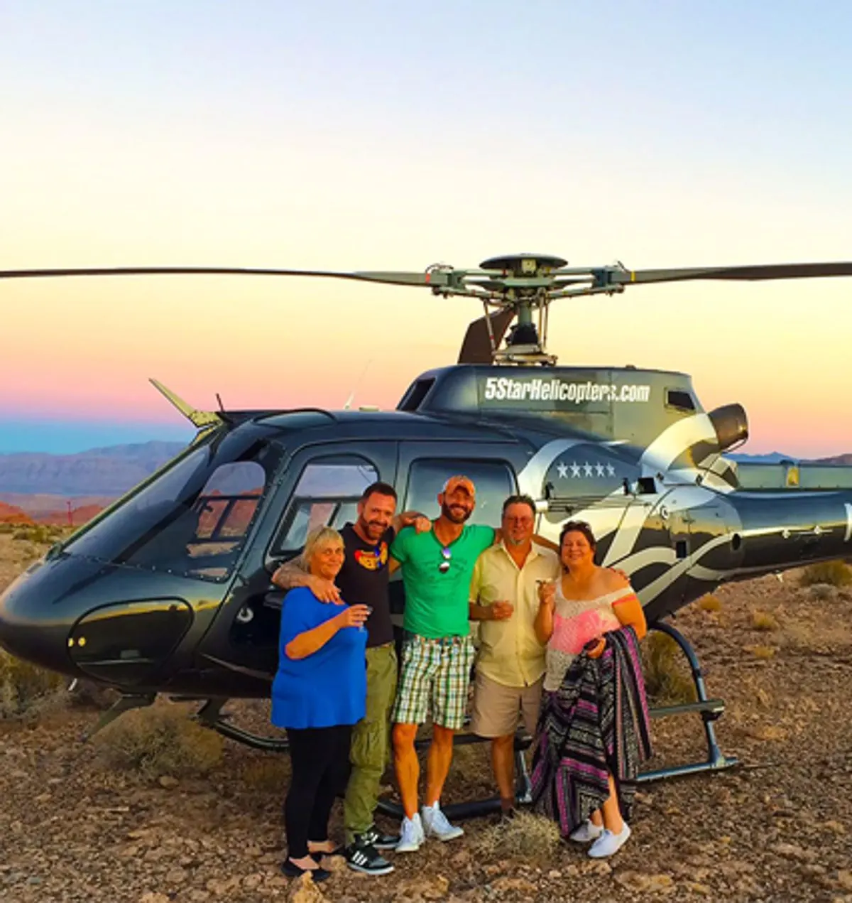 Group of five guests with champagne beside a 5 Star helicopter at sunset
